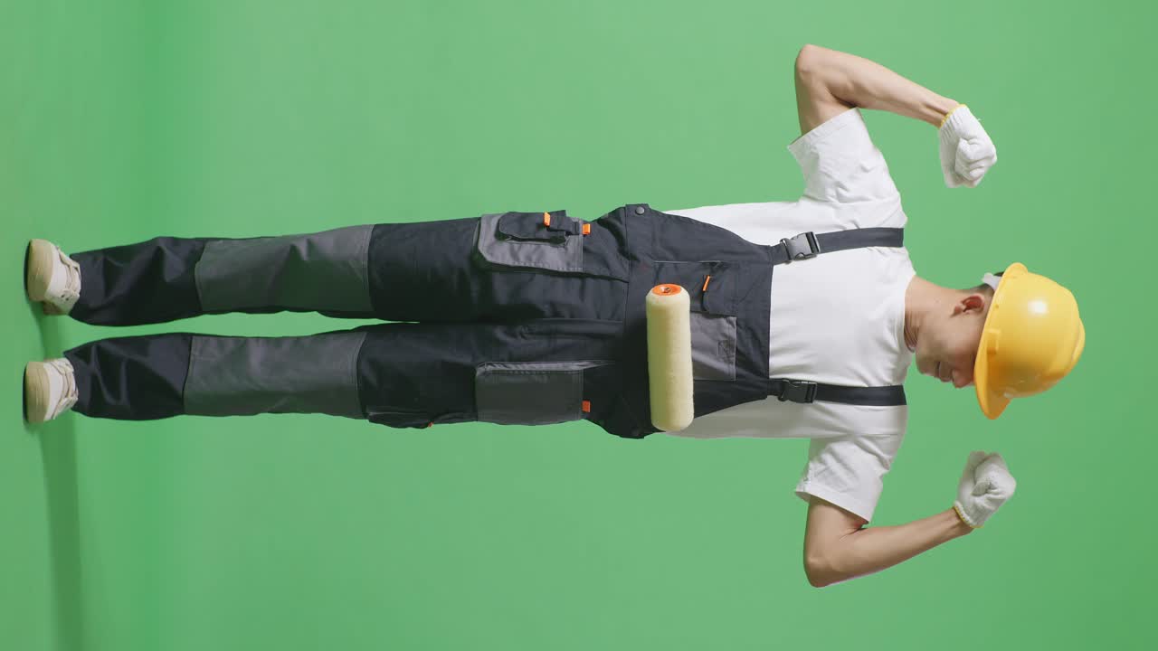 Full Body Of Asian Man Painter Wearing Safety Helmet Smiling And Flexing His Bicep While Standing In The Green Screen Background Studio