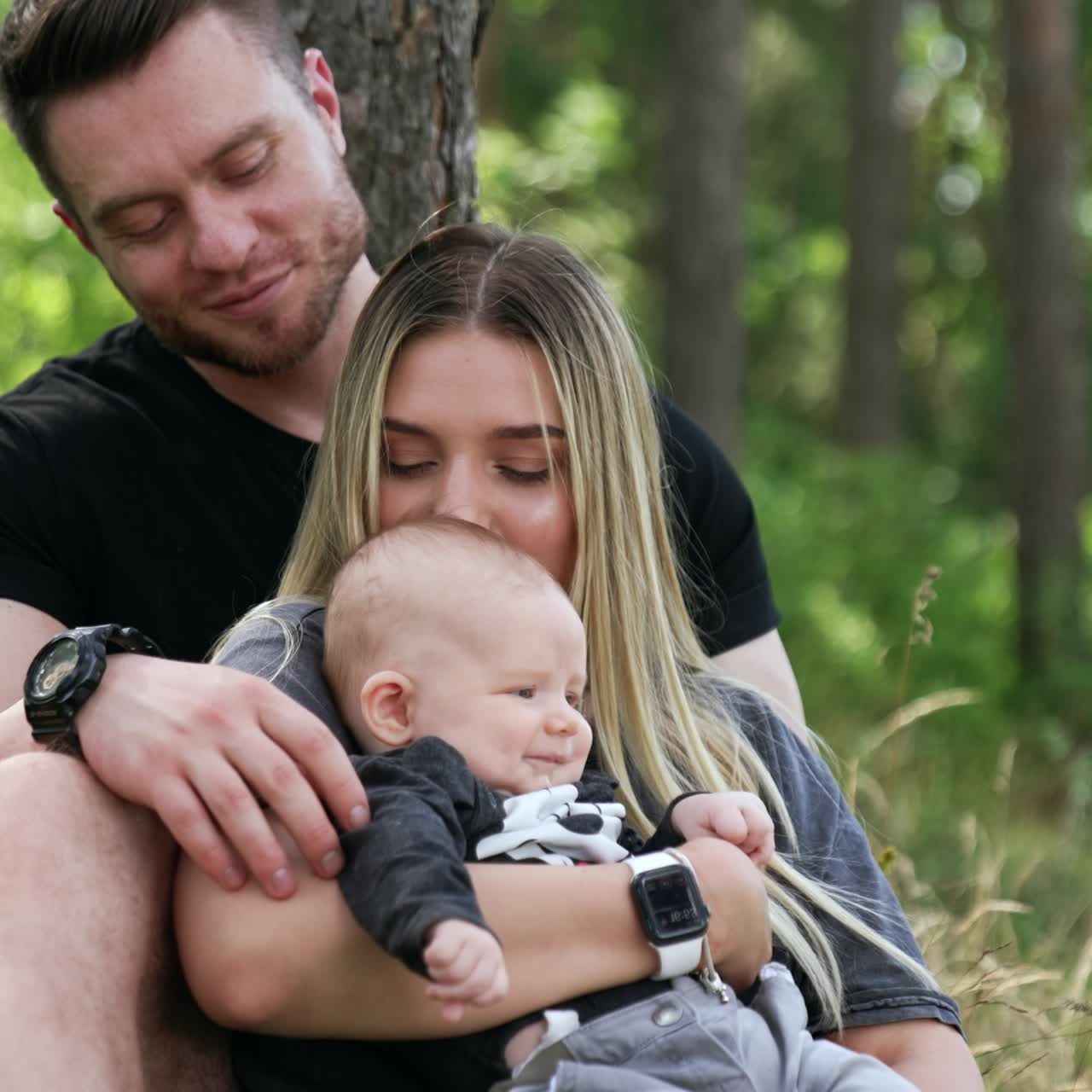 Una famiglia caucasica di tre persone seduta nel bosco. La donna bacia il suo bambino sulla testa