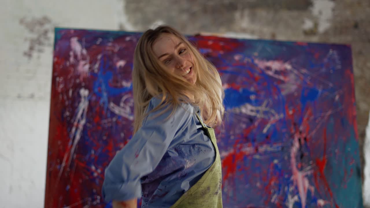 Donna che balla in modo divertente davanti a un dipinto astratto nello studio, al rallentatore.