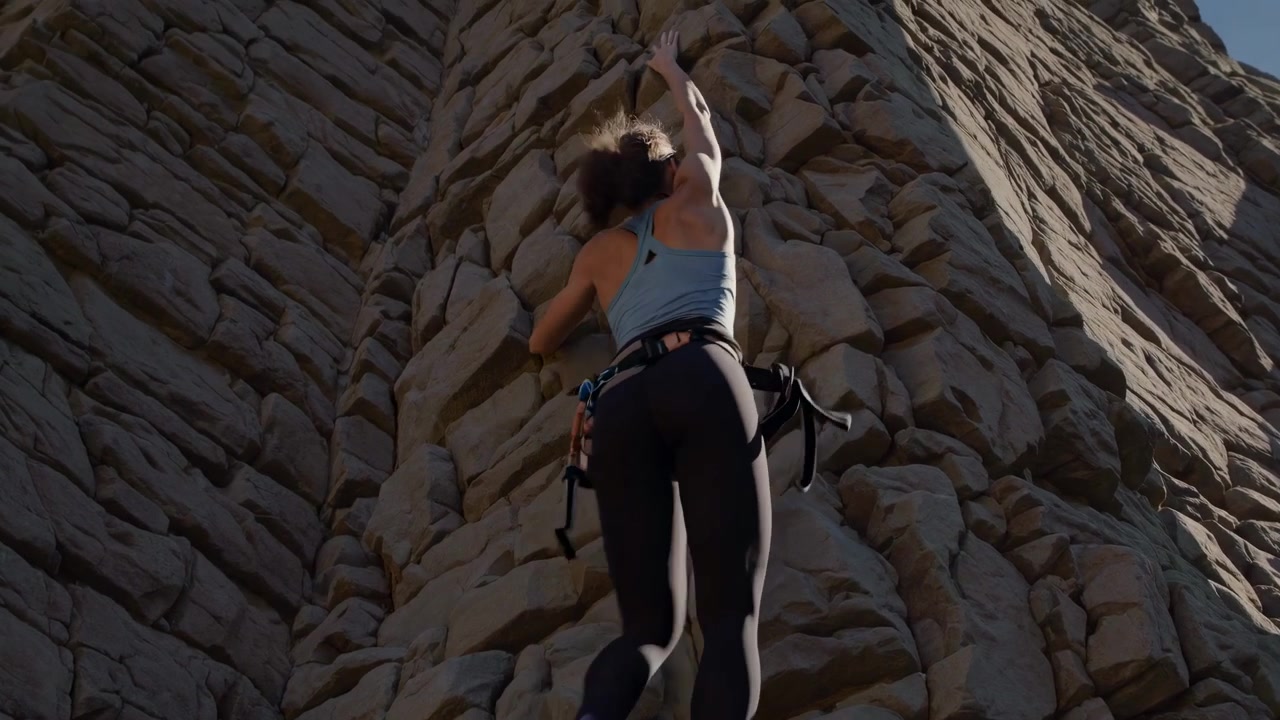 Jovem mulher praticando escalada em uma parede rochosa natural e íngreme