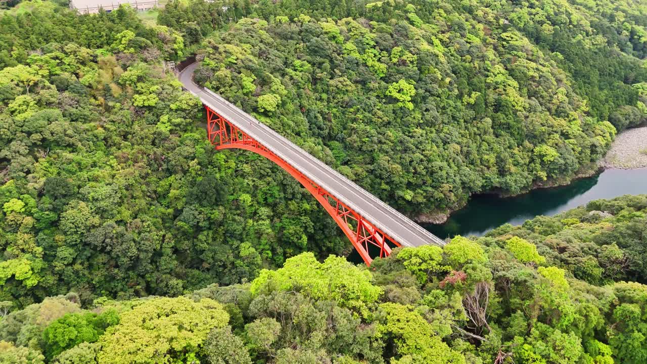 Scenic aerial view of a red bridge over a river surrounded by lush forest