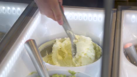 Hand-scooping-vanilla-ice-cream-from-display-case-into-cup,-closeup