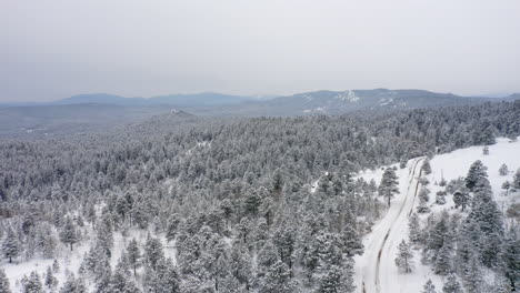 Vista-Aérea-De-Drones-De-Carreteras-Secundarias-Nevadas-Sin-Arar-En-Colorado-Rodeadas-De-Bosques-De-Pinos-Cubiertos-De-Nieve-Y-Hielo-Después-De-La-Tormenta-De-Invierno