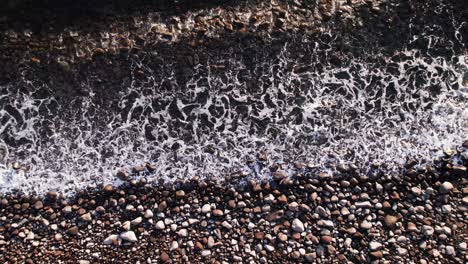 Luftaufnahme-Von-Oben-Nach-Unten-Von-Meereswellen,-Die-Auf-Dem-Schwarzen-Kopfsteinstrand-Rollen