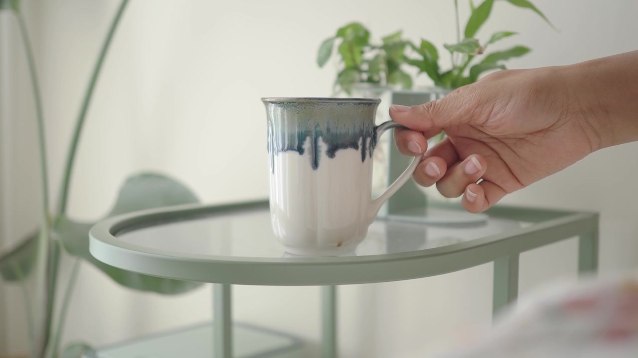 Mão Pegando uma Caneca de Cerâmica de uma Mesa Lateral
