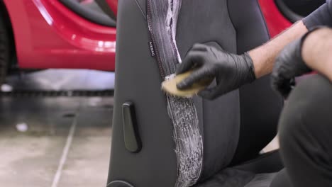 the specialist is engaged in dry cleaning of the removed car seat. mechanic rubbing foam into fabric. stage of complete dry cleaning of the car. detailing center services.