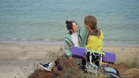 couple of backpack tourists sitting at cliff embraced, enjoying breathtaking view of sea