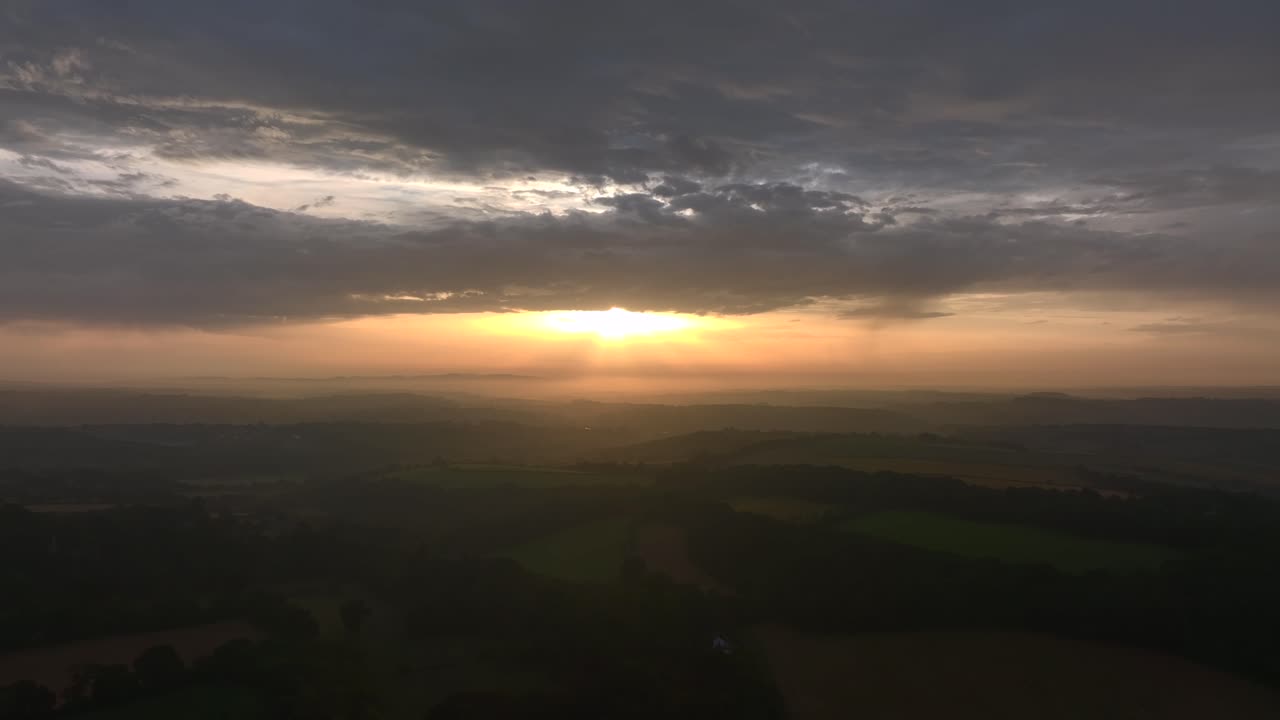 Daybreak over rural English countryside with misty horizon. Slow panning and upward tilt shot. Summer. Cornwall, UK.
