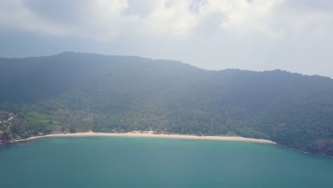 Aerial-view-above-ocean-towards-incredible-island-with-beach-and-trees-in-Thailand---camera-tracking-pedestal-down