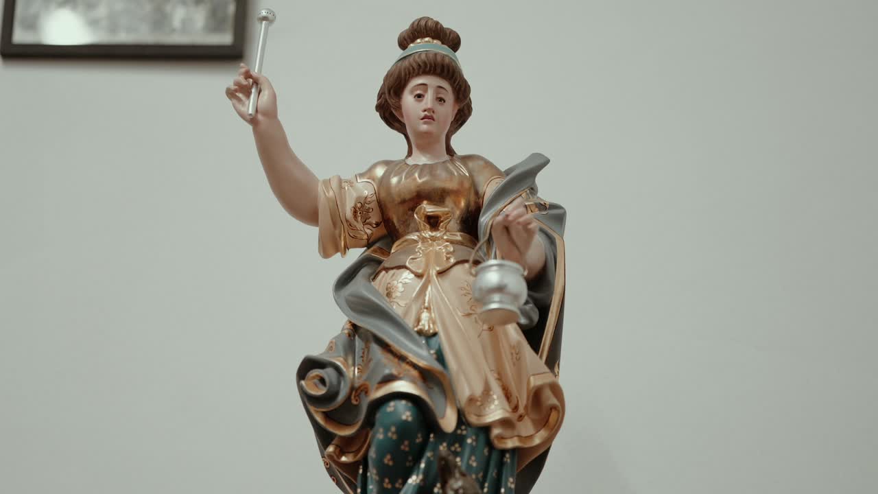 Close view of female saint sculpture with lantern and staff indoors