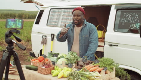 positive black farmer selling vegetables and filming ad with smartphone