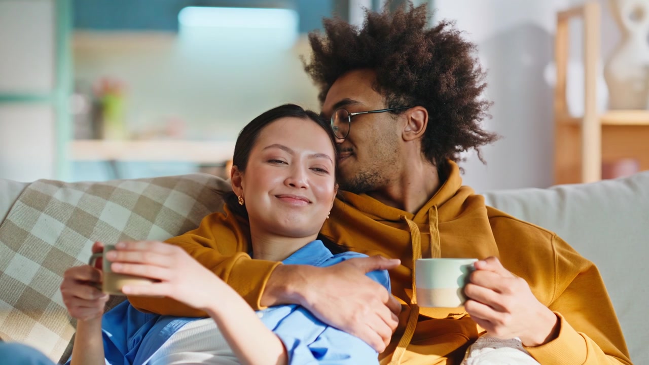 Coppia affettuosa che beve caffè sul divano di casa. Primo piano di una coppia felice che si rilassa