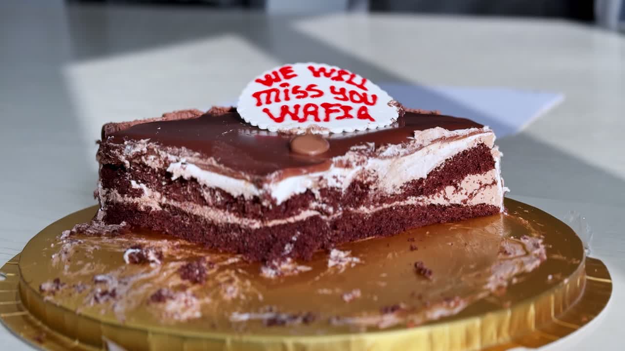 Sjokoladeavskjedskake med personlig melding på et gullfat inne på et lyst kontor. Desserten har kremfyll og fyldig glasur under en avskjedsfest.