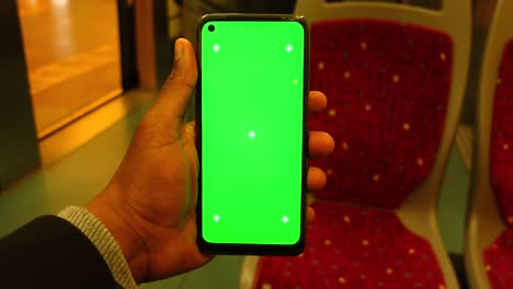 person holding a smartphone with a green screen on a bus