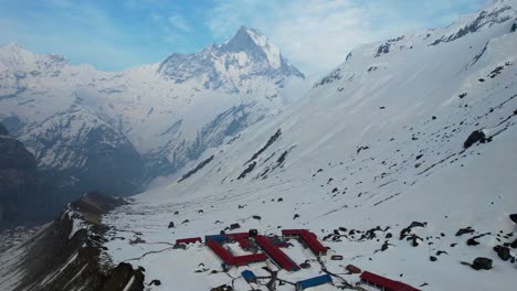 aerial flying over annapurna base camp on snow covered mountain side with machapuchare peak in background