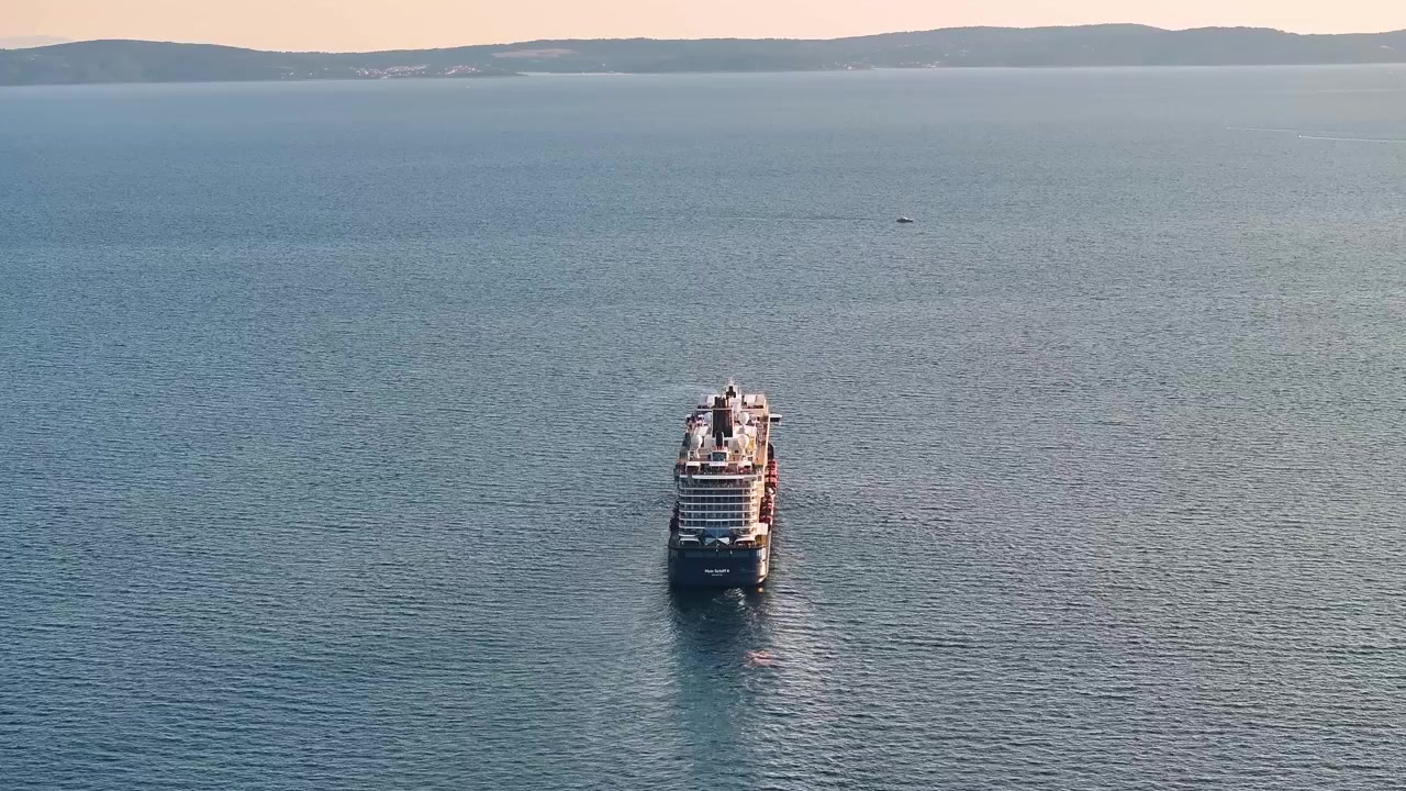 Kruvaziyer gemisi açık sularda seyrederek bir sahil şehrine doğru ilerliyor. Turistler modern bir yolcu gemisinde yolculuklarının tadını çıkarıyor.
