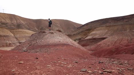 Adventurer-walking-up-the-hill,-arid-and-colorful-landscape,-Israel-desert,-cloudy-day,-static-shot