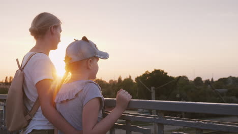 A-Woman-With-Her-Daughter-Are-Standing-At-The-Railing-Of-The-Bridge-At-Sunset-Evening-Walk-With-Mom