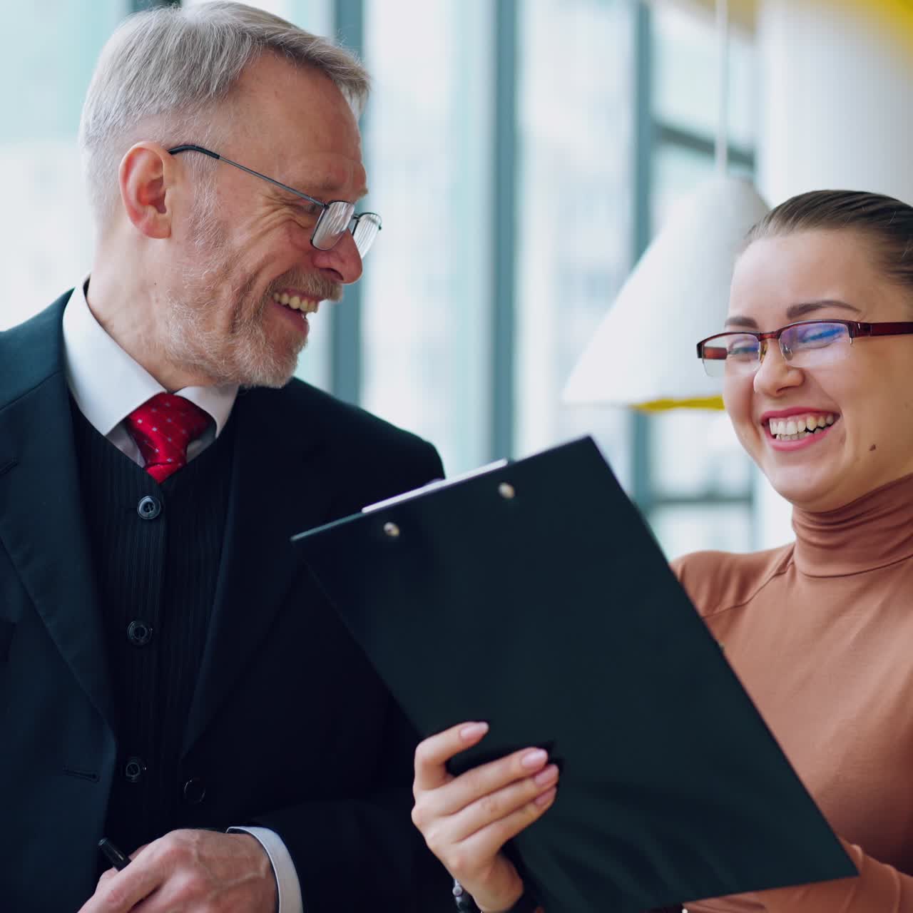 Smiling old businessman and a female secretary. Young woman talking with a mature man in costume in the modern office.