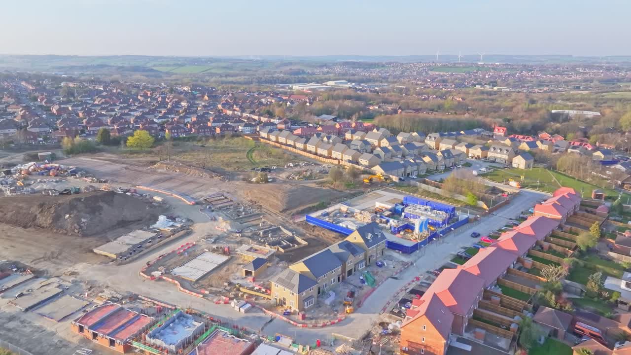 Wide aerial drone pan revealing a large housing construction site, new residential streets, and the surrounding suburban landscape in Wombwell, South Yorkshire, England