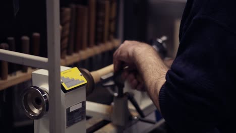 carpenter male hands cutting wooden knob out of wood piece spinning on machine using chisel, working on the form, decoration. slow motion. side view