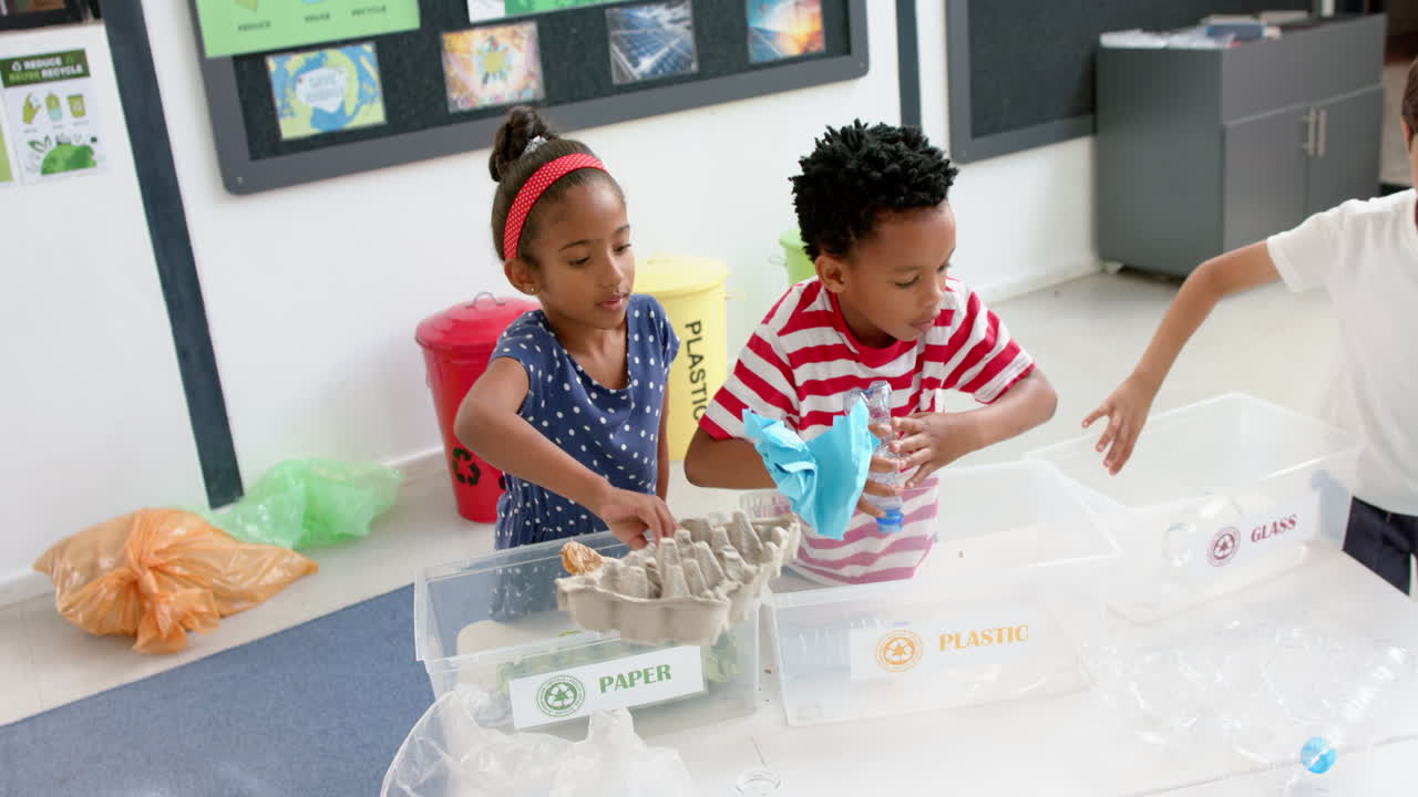 In school, children sorting recyclables into paper, plastic, and glass bins