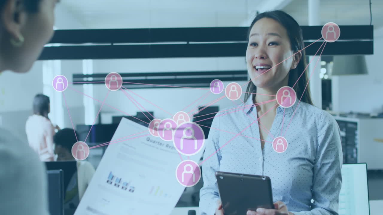 Animation of connected icons over diverse female coworkers discussing reports in office