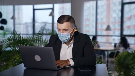 man wearing surgical mask works in an office in front of laptop. employer closes his laptop, takes off his mask and throws it backwards. office work during pandemic times.