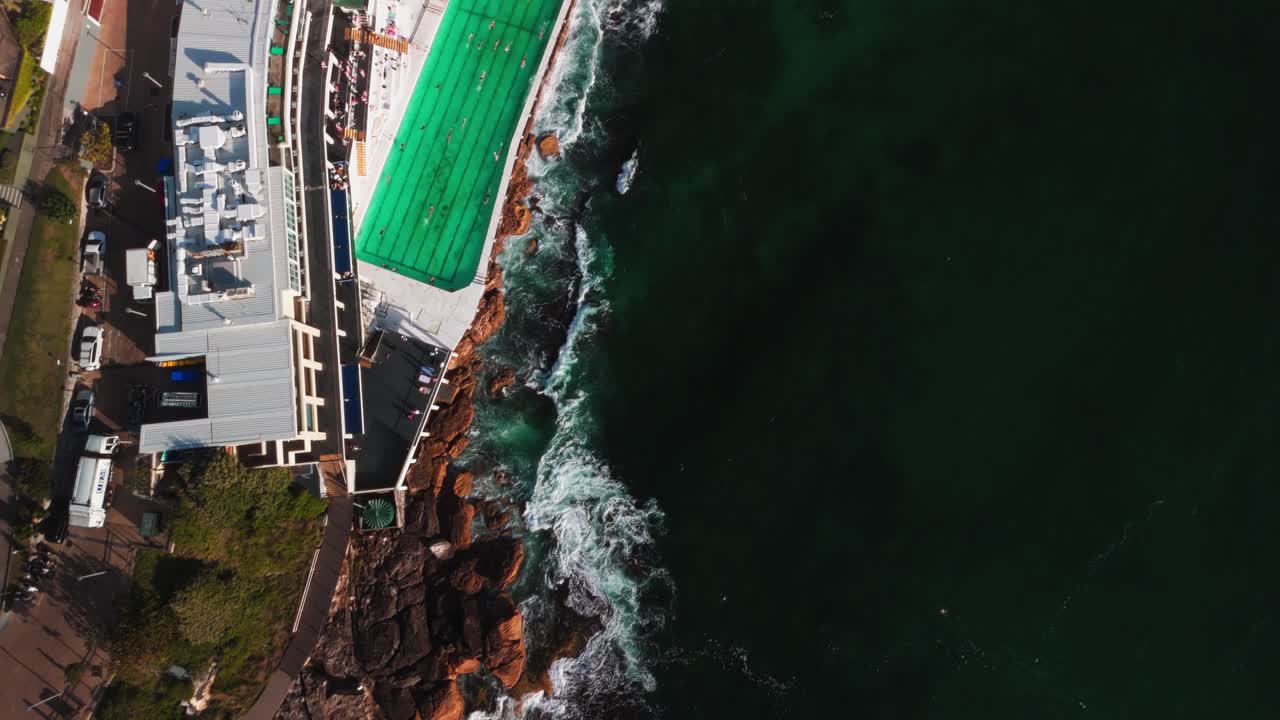 보디 아이스버그의 수영장을 위에서 찍은 드론 사진은 수영객과 바위가 있는 해안선에 파도가 부히는 모습을 보여줍니다. 수영장과 어두운 바다의 대조는 눈에 띄고 있습니다.