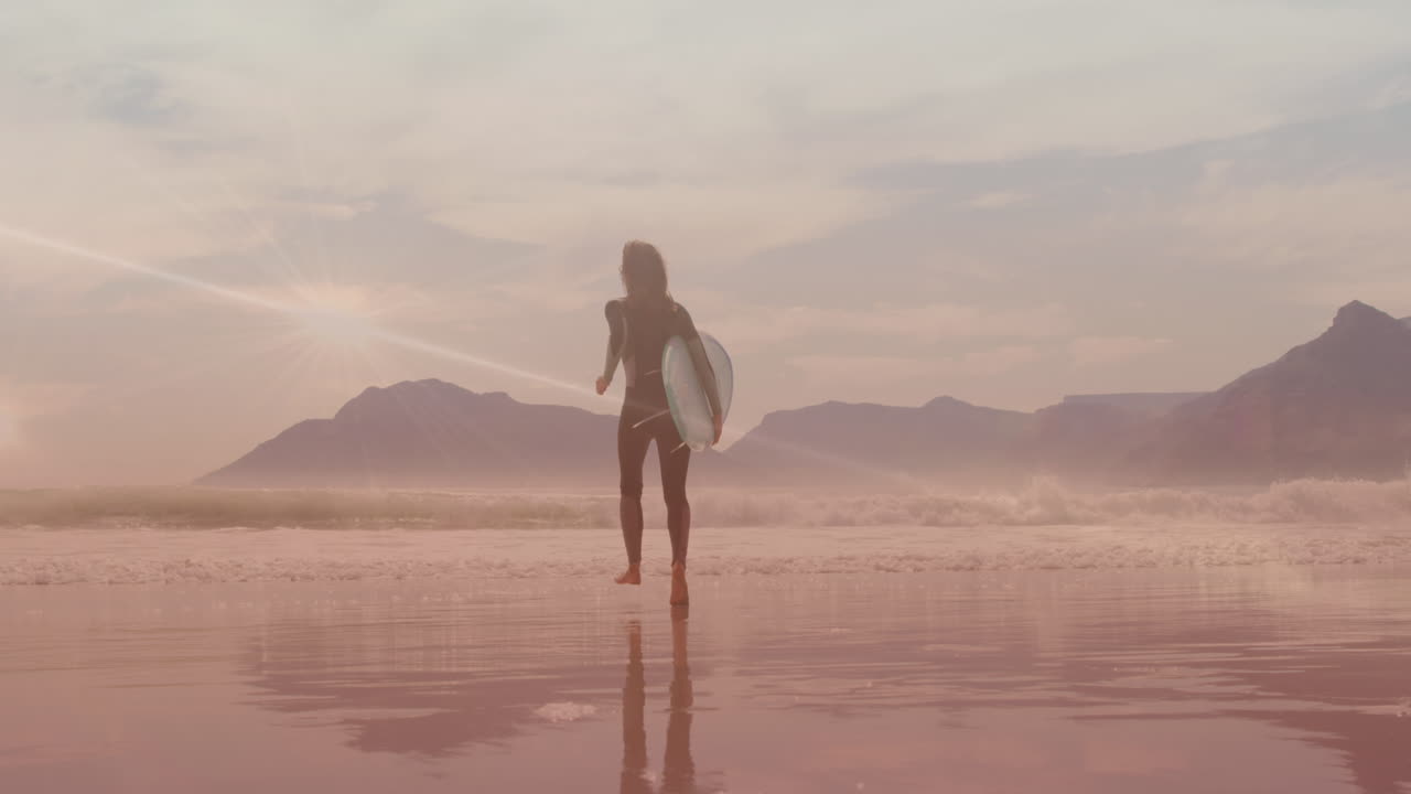 Animation af lysspor over kaukasisk kvinde der går med surfbræt på stranden