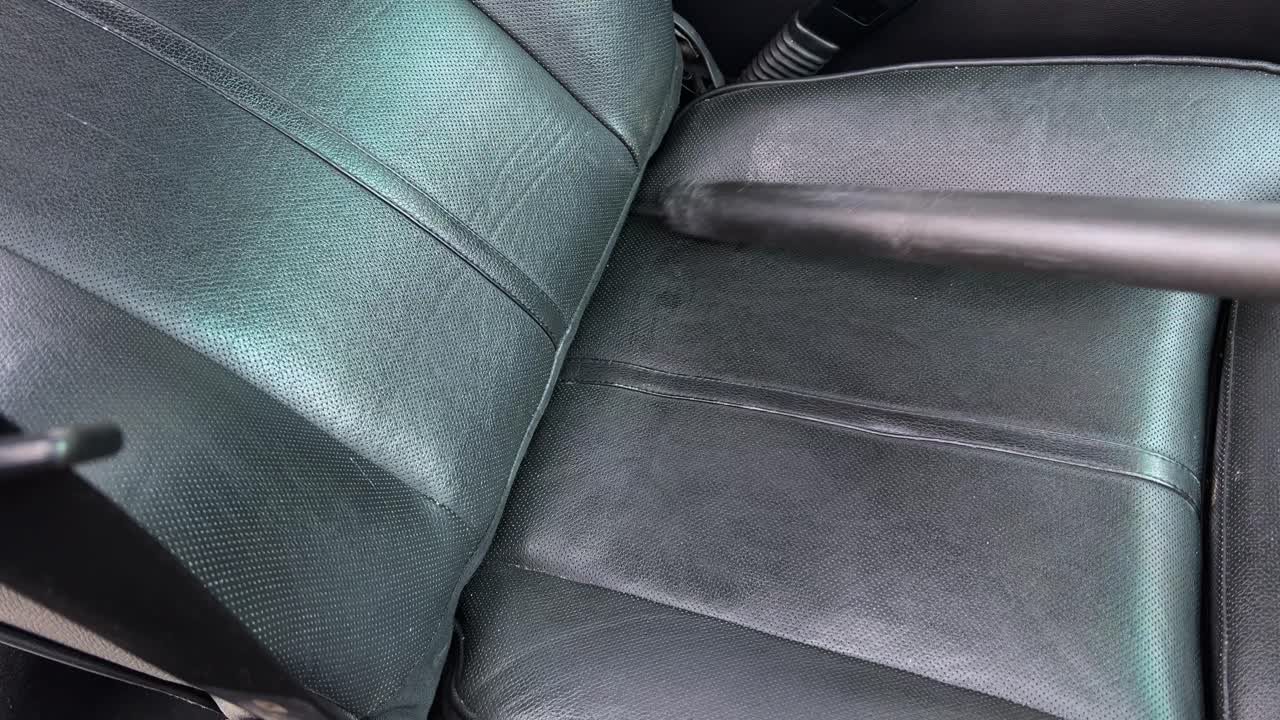 Vacuuming out dirty car floors and black leather seats interior in crack of passenger seat of black leather electric seat as it&rsquo;s raised back up after cleaning