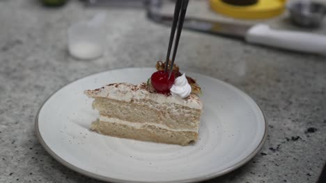 un chef de pastelería profesional coloca una cereza en una pieza de pastel preparando una receta de postre en la cocina del restaurante