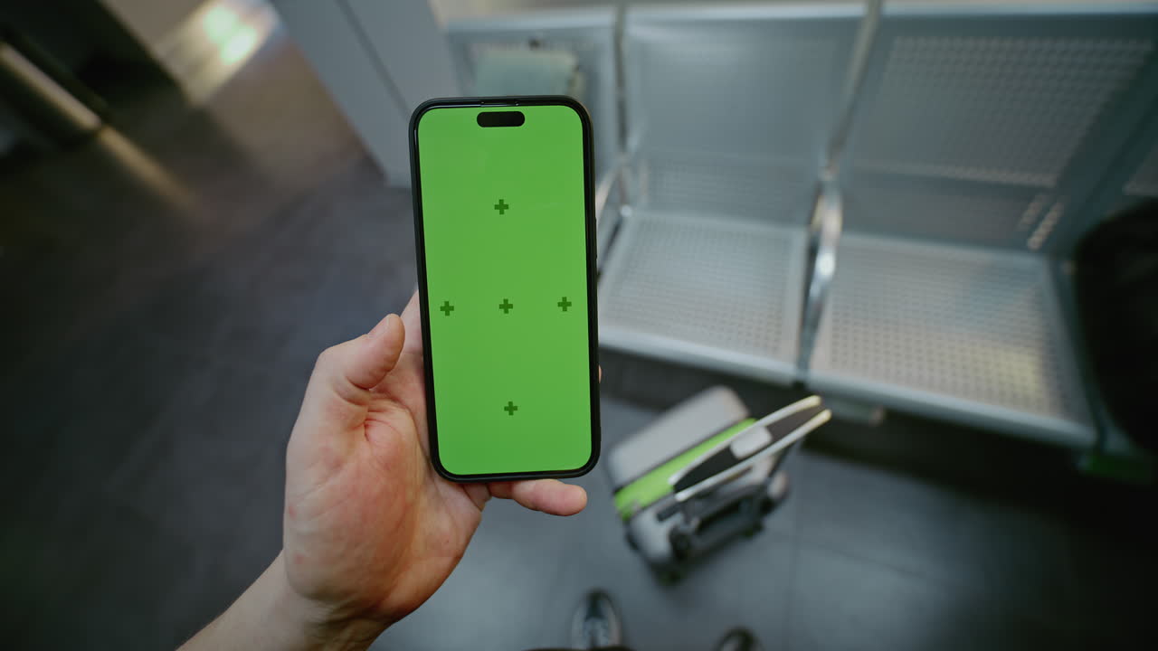 Person holding a smartphone with a green screen in a train station