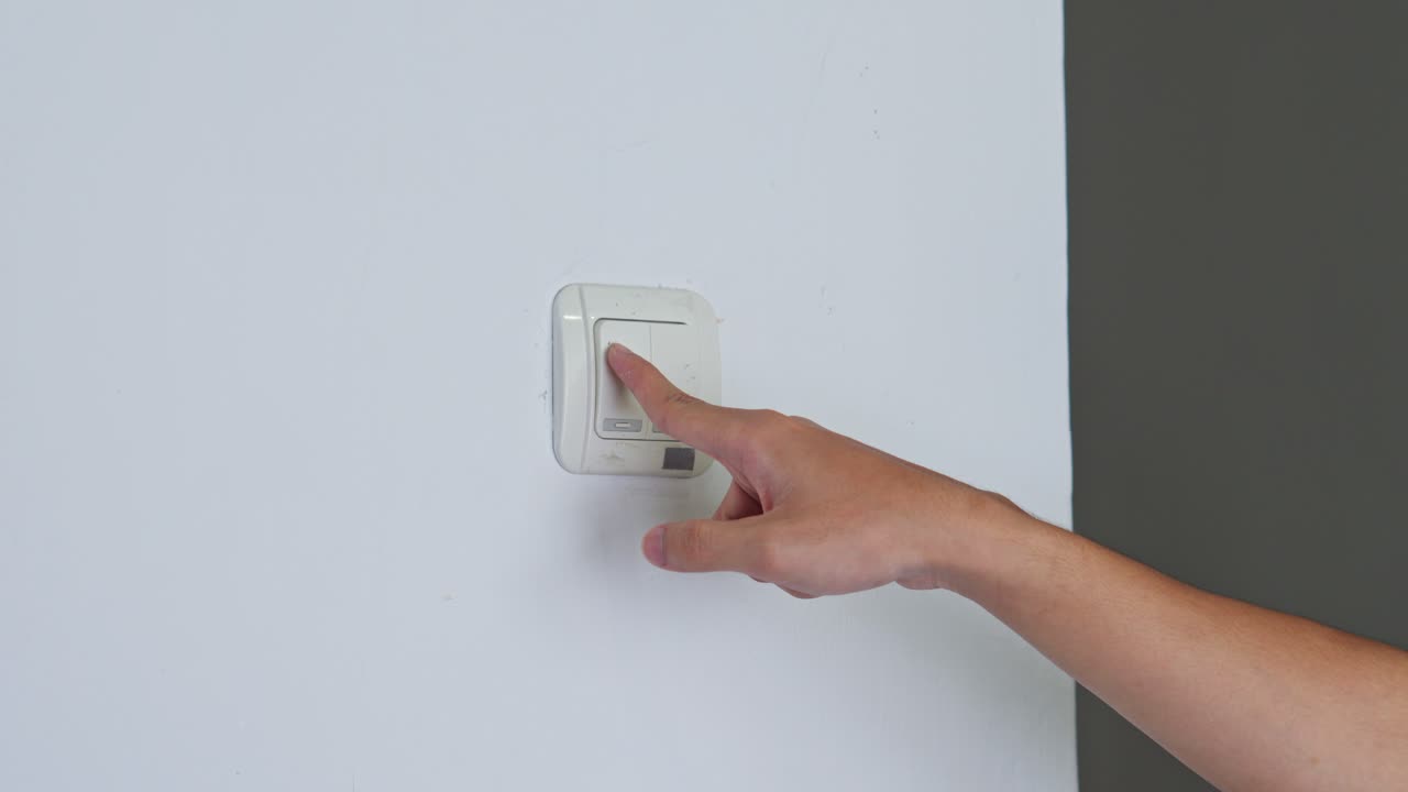 Person's hand pressing wall light switch to turn off power