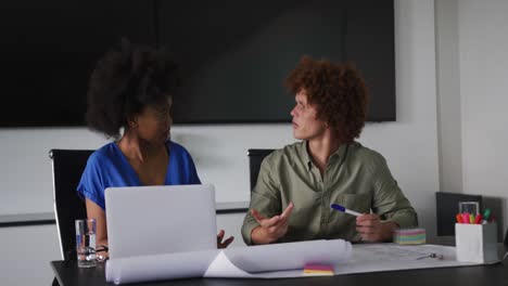 diverse male and female business colleagues in discussion at work using laptop computer