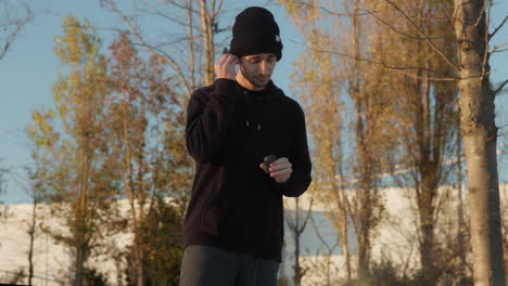 Young-Man-Putting-Earphones-In-And-Getting-Ready-For-A-Run,-Medium-Wide-Shot