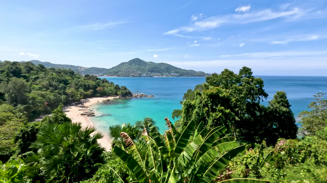 Lush green foliage, turquoise sea, and sandy coastline under bright daylight with smooth panoramic movement