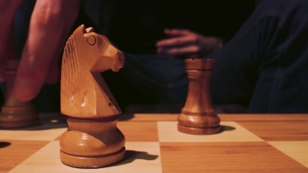 Following shot of a hand playing a chess piece on a giant looking chess board.