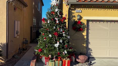 árbol de navidad con decoración y cajas con regalos fuera de casa en un día soleado