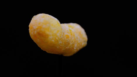 cheesy puff snack food turning slowly, isolated on black background - close up