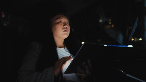 business chinese woman driving in a taxi and browsing digital tablet at night.