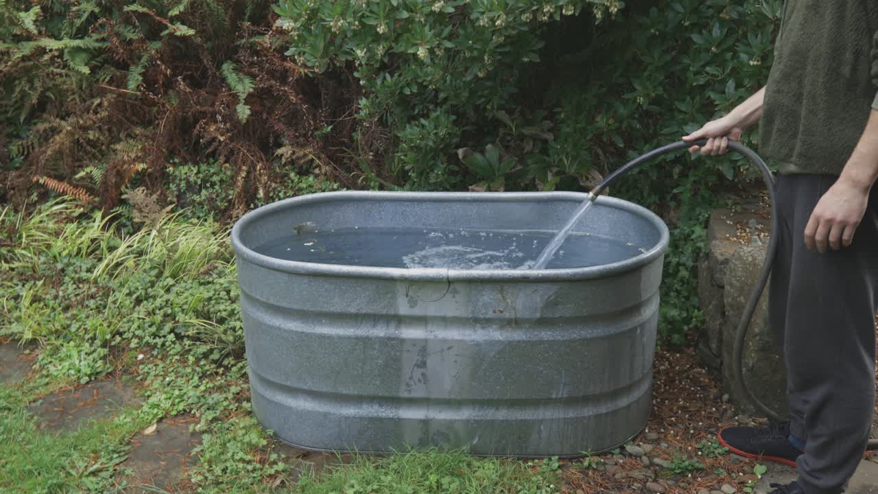 콜드 플런징을 위한 외부 욕조에 물을 채우는 동안 호스를 들고 있는 미국 남자