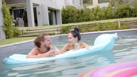 a young caucasian couple relaxes in a pool with drinks