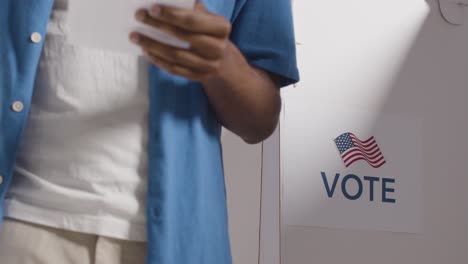 close up of man next to booth with ballot paper in american election deciding how to cast his vote