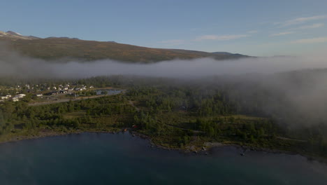 clouds and fog over sjodal lake, village and jotunheimen national park in norway. - aerial