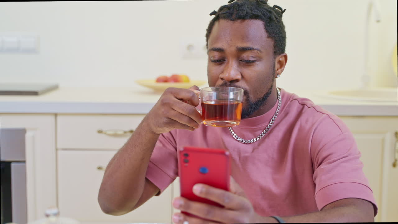 hombre bebiendo té y usando un teléfono en la cocina