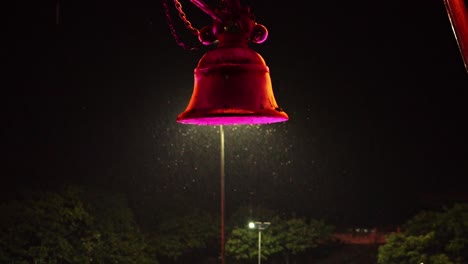 swarm of insects flying around a colorful glowing bell on a rainy night - close up