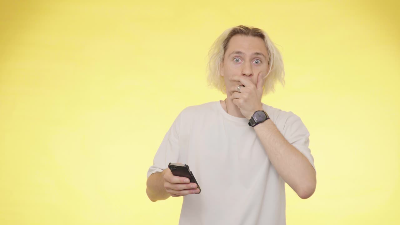 un joven guapo mira su teléfono y está muy sorprendido por las buenas noticias