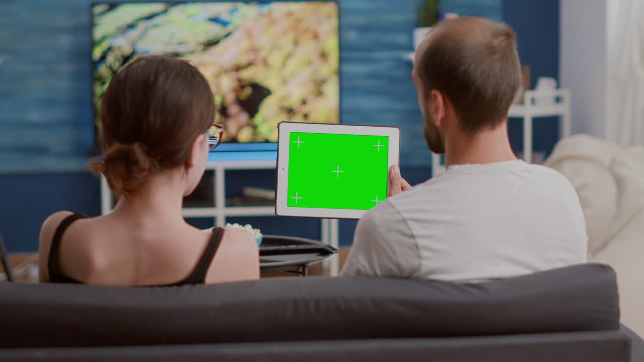 Static tripod shot of man and woman couple watching influencer vlog using digital tablet with green screen