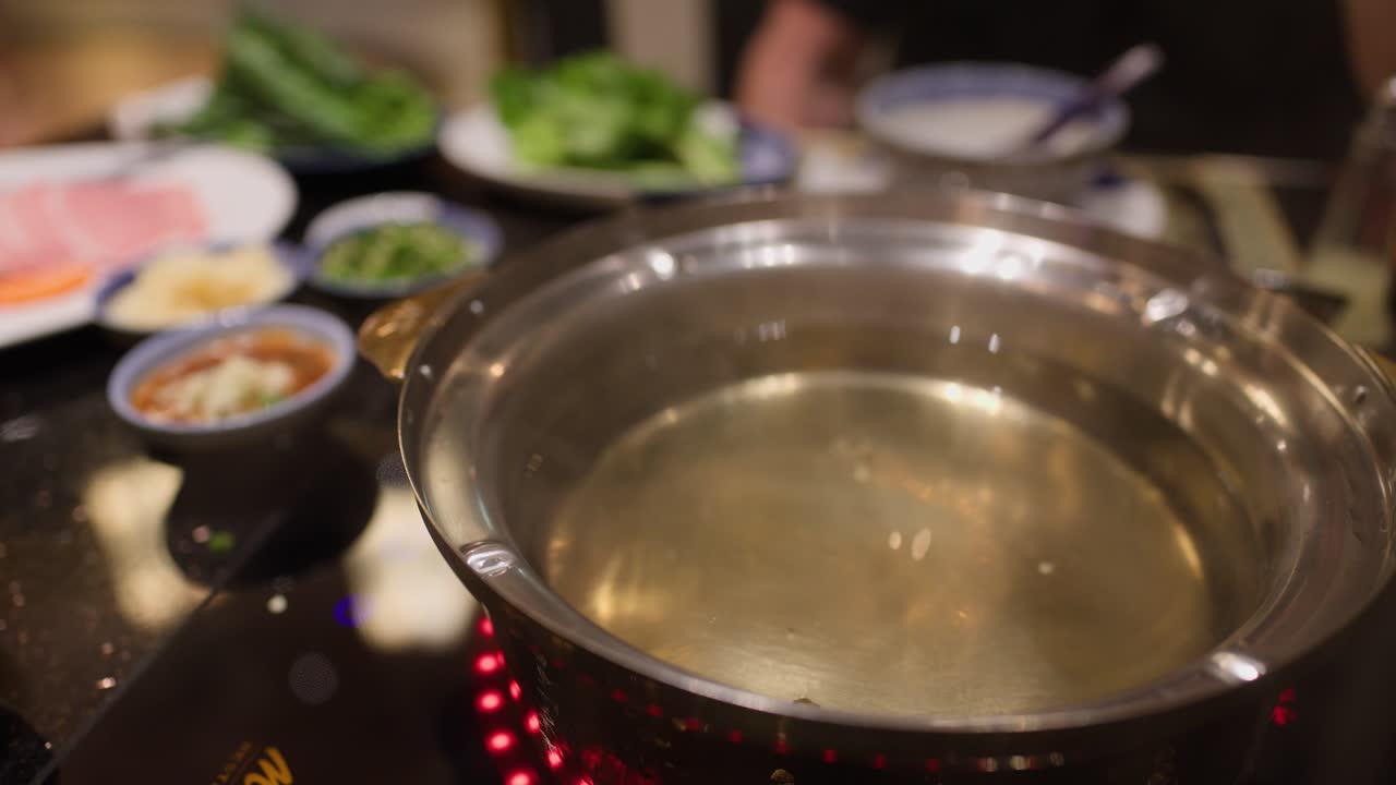 Simmering clear hotpot broth on induction stove, surrounded by fresh ingredients under warm lighting